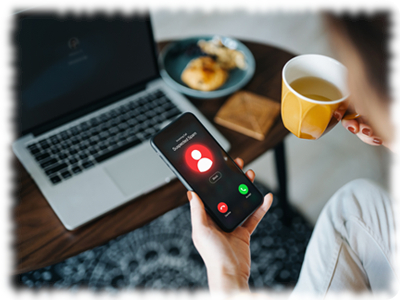 Immagine raffigurante un computer portatile sullo sfondo e una donna intenta a bere un caffè, con in mano uno smartphone e un messaggio ben visibile di allerta sullo schermo